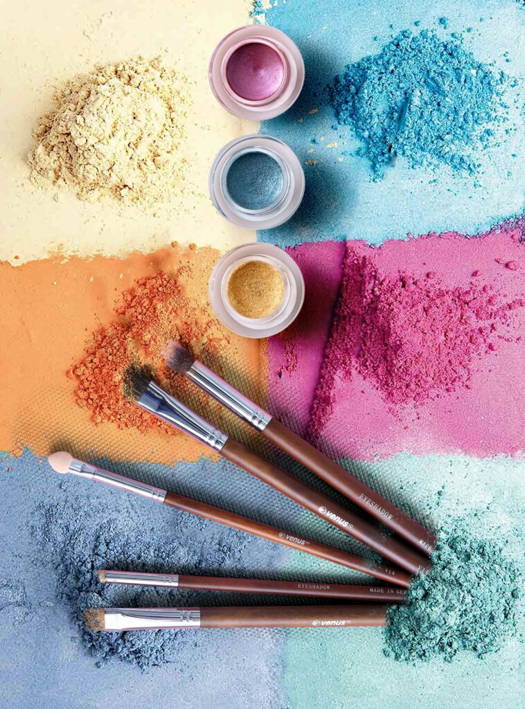 Colorful makeup powders and brushes in an artistic flat lay composition.